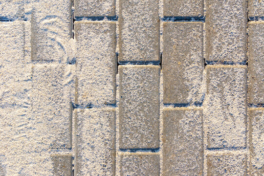 Close-up of rectangular concrete pavers laid in a brick-like pattern with light sand filling the gaps.